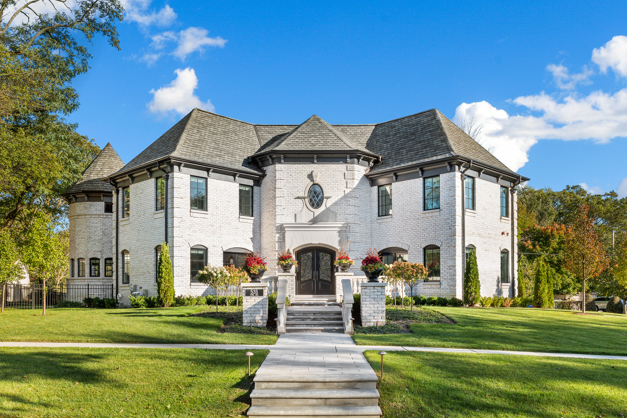 Exterior front view of white brick custom home with hip roof. Showing lawn, entry and turret.