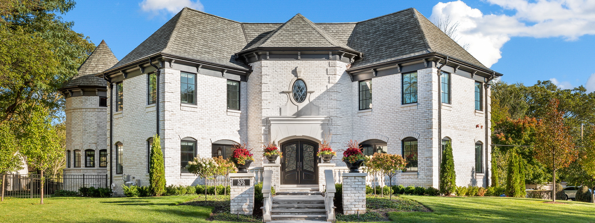 Front of white brick, two-story luxury custom home with hip roof, double door entry, terrace and tourelle